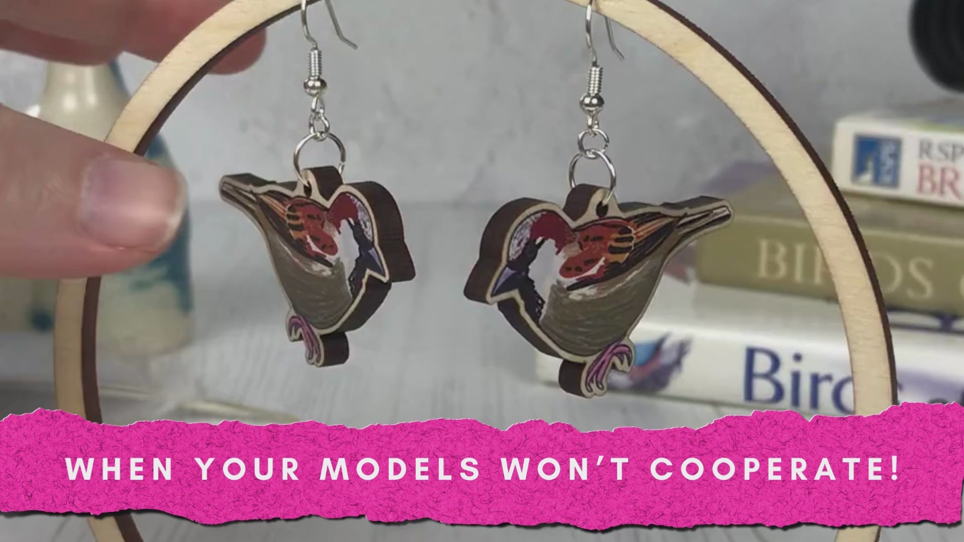 Load video: A video of laser cut wooden statement earrings by Loadofolbobbins showing illustrations of sparrows on them. They&#39;re dangling from a circular hoop earring stand and are being repeatedly adjusted by two hands. Text on the video says when your models won&#39;t cooperate!